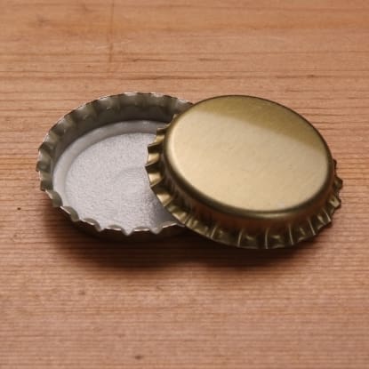 Two gold bottle caps on wood table.